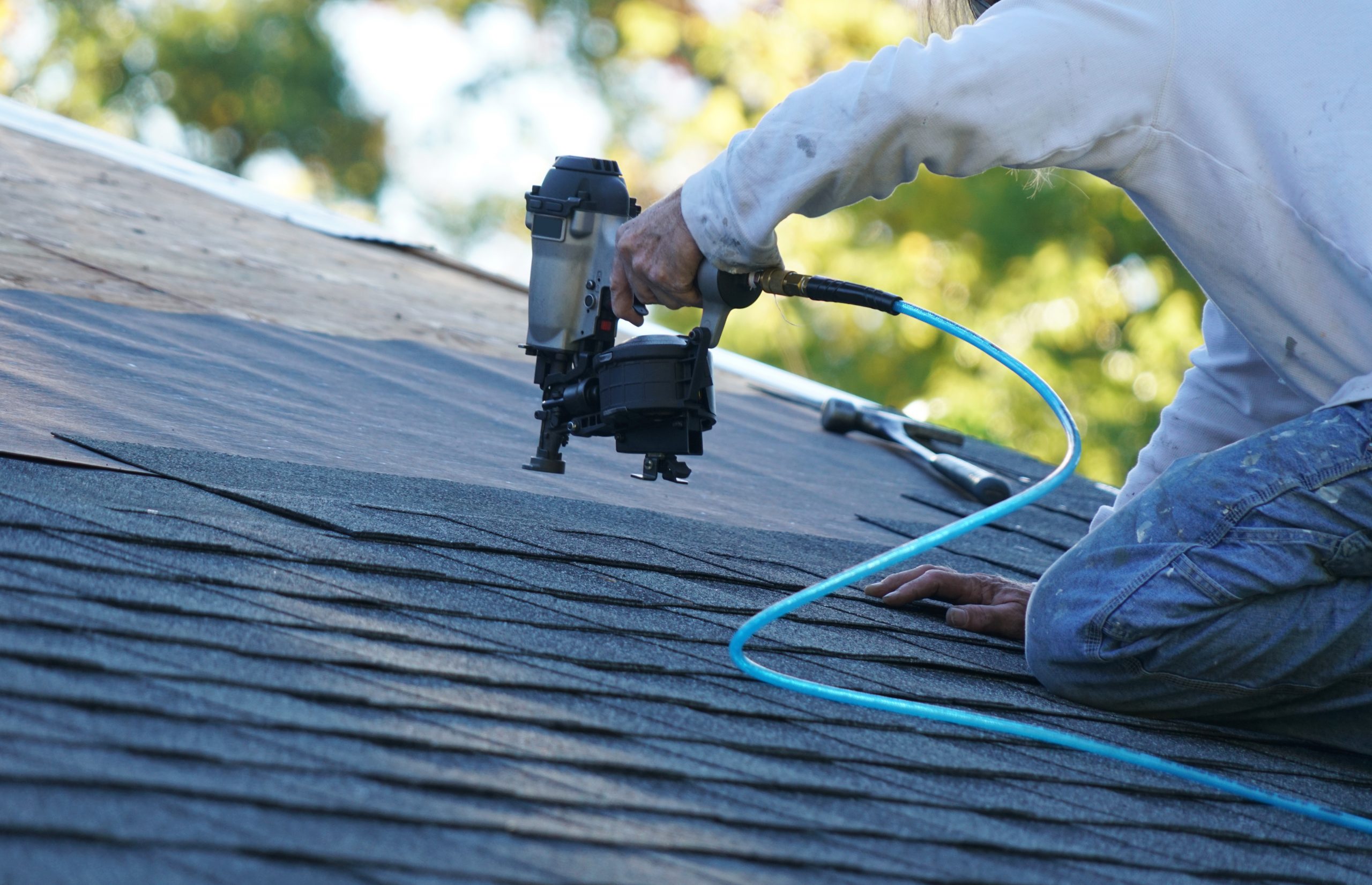 handyman using nail gun to install shingle to repair roof